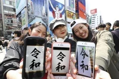 Các cô gái giới thiệu tên niên hiệu mới của Nhật Bản trên màn hình điện thoại ở Osaka ngày 1/4. (Ảnh: Kyodo/TTXVN) 