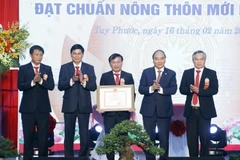 Chủ tịch nước Nguyễn Xuân Phúc trao Bằng chứng nhận huyện đạt chuẩn nông thôn mới cho lãnh đạo huyện Tuy Phước. (Ảnh: Thống Nhất/TTXVN)