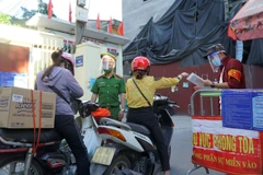 Thành viên Tổ COVID-19 cộng đồng đang cùng lực lượng công an kiểm tra người dân ra vào khu vực chốt phong tỏa. (Ảnh: Minh Hiếu/Vietnam+)