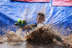 Nhiều người phải cởi giày để trượt xuống hố bùn vì khả năng cao sẽ mất giày. (Ảnh: Minh Sơn/Vietnam+)