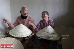 Những hình ảnh ấn tượng các bà, các chị, đang ngồi khâu nón lá, miệng cười nói vui vẻ khiến du khách rất thích thú. (Báo ảnh Việt Nam/Vietnam+)