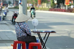 Người bán vé số dùng quạt tích điện khi ngoài trời nắng nóng. (Ảnh: Phan Tuấn Anh/TTXVN)