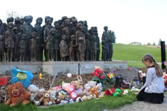 Bé Tina đặt cành hoa trắng trước cụm tượng trẻ em. (Ảnh: Trần Quang Vinh/Vietnam+)