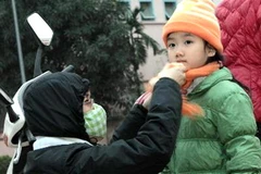 Phụ huynh chủ động mặc ấm cho con em khi đến trường. (Ảnh: Bích Ngọc/TTXVN)