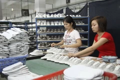 Công đoạn dán keo sản phẩm giầy trẻ em. (Ảnh: Hoàng Hùng/TTXVN)