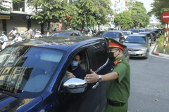 Lực lượng chức năng kiểm tra giấy tờ tuỳ thân và xác nhận đi làm, ra ngoài của cơ quan với người dân lưu thông trên đường Đào Tấn, Hà Nội (sáng 28/7/2021). (Ảnh: Lâm Khánh/TTXVN)