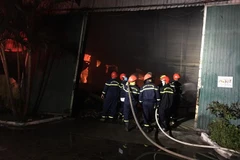 Lực lượng chức năng nỗ lực để đám cháy không lan sang các nhà kho khác liền kề. (Ảnh: Đỗ Trưởng/TTXVN)