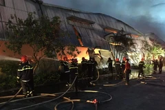 Lực lượng chức năng nỗ lực để đám cháy không lan sang các nhà kho khác liền kề. (Ảnh: Đỗ Trưởng/TTXVN)