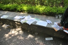 Hàng chục loại tờ rơi được dúi vào tay các vị phụ huynh tạo nên khung cảnh không mấy đẹp mắt tại điểm thi. (Ảnh: Võ Phương/Vietnam+)