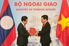 Phó Thủ tướng, Bộ trưởng Ngoại giao Phạm Bình Minh và Bộ trưởng Ngoại giao Lào Saleumxay Kommasith trao đổi tượng trưng hai ấn phẩm văn kiên pháp lý biên giới Việt Nam-Lào. (Ảnh: Nguyễn Khang/TTXVN)