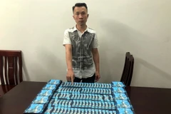 Đối tượng Trần Anh Dũng cùng tang vật 100 sản phẩm thuốc lá điện tử có chứa chất ma túy MDMB-4en-PINACA. (Ảnh: TTXVN phát)