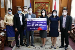 Ông Nguyễn Đức Vũ (Trái) Tổng Giám đốc Ngân hàng Liên doanh Lào - Việt đang trao tượng trưng số tiền 50.000.000 kip (Khoảng 115 triệu đồng) ủng hộ Quỹ vaccine phòng chống COVID-19 của Việt Nam cho Công sứ Trịnh Minh Tâm. (Ảnh: Phạm Kiên/TTXVN)
