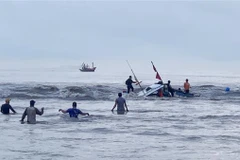 Lực lượng chức năng cùng người dân nỗ lực trục vớt, lai dắt thuyền đánh cá bị nạn vào bờ. (Ảnh: TTXVN phát)