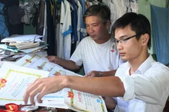 Thủ khoa Trần Hữu Chí và bố bên những tấm giấy khen mà Chí giành được trong 12 năm học phổ thông. (Nguồn: Dân Trí)