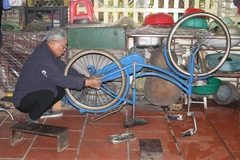 Ông Lê Trọng Kính sửa xe đạp cũ để tặng học sinh nghèo. (Ảnh: Thùy Dung/TTXVN)
