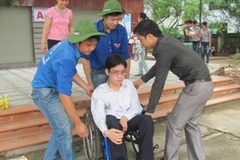 Sinh viên tình nguyện giúp Hoàng khiêng xe lăn. (Ảnh: Phạm Mai/Vietnam+)