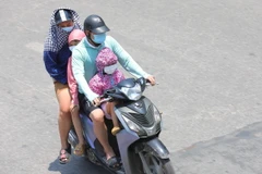 Một gia đình phải mặc áo chống nắng khi phải di chuyển trên đường. (Ảnh: Hoàng Hiếu/TTXVN)