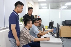 Anh Vũ Văn Hạnh (ngồi ở giữa) trao đổi với các đồng nghiệp về ứng dụng Phản ánh kiến nghị trên thiết bị di động. (Ảnh: Thanh Thương/TTXVN)