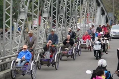 Khách du lịch hết sức thích thú khi đi xích lô tham quan cầu Tràng Tiền và hệ thống di tích Cố đô Huế. (Ảnh: Quốc Việt/TTXVN)