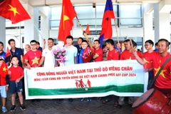 Các cổ động viên và cộng đồng người Việt Nam tại Lào chụp ảnh kỷ niệm với Huấn luyện viên Kim Sang-sik và một số cầu thủ đội tuyển Việt Nam bên ngoài sảnh đến tại sân bay quốc tế Wattay, ngày 6/12/2024. (Ảnh: Xuân Tú/TTXVN)