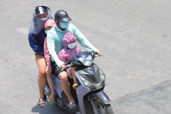 Một gia đình phải mặc áo chống nắng khi phải di chuyển trên đường Giải Phóng lúc 11h40. (Ảnh: Hoàng Hiếu/TTXVN)