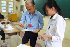 Giám thị kiểm tra thông tin của thí sinh trước khi vào phòng thi Trung học phổ thông quốc gia. (Ảnh: PM/Vietnam+)