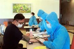 Nhân viên y tế hướng dẫn chuyên gia, lao động nước ngoài khai báo y tế và kiểm tra sức khỏe trước khi vào khách sạn cách ly. (Ảnh: TTXVN)