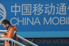 Một người sử dụng iPhones 5s đứng trước biển quảng cáo China Mobile ở Thượng Hải (Nguồn: TTXVN)