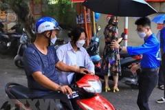 Lực lượng thanh niên tình nguyện che ô cho thí sinh tại điểm thi Trường THPT Kim Liên, quận Đống Đa. (Ảnh: Hoàng Nguyên/TTXVN)