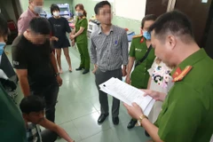 Cán bộ công an đọc quyết định bắt giữ bị can, lệnh khám xét đối với Trần Công Xuân. (Ảnh: TTXVN phát)