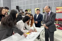 Những người tham gia hội chợ ký tên bày tỏ tình cảm của mình lên chiếc áo có hình cờ Việt Nam, sẽ được gửi tới Phòng truyền thống tại huyện đảo Trường Sa. (Ảnh: Nguyễn Thu Hà/TTXVN)