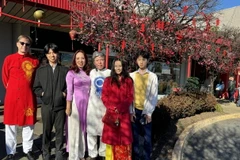 Gia đình chị Thảo anh James chụp ảnh bên cây đào cảnh tại khu chợ Việt. (Ảnh: Kiều Trang/TTXVN)