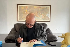 Họa sỹ Thành Chương ký tên lên cuốn sách của nhà văn Kim Lân. (Ảnh: Minh Thu/Vietnam+)