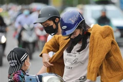 Người đi đường dừng xe để mặc thêm áo ấm. (Ảnh: Thanh Tùng/TTXVN)