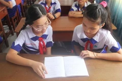 Em Võ Ngọc Gia Bảo (bên trái) trao đổi bài học với bạn cùng lớp. (Ảnh: Hữu Chí/TTXVN)