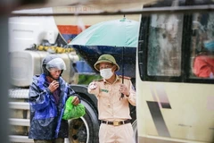 Lực lượng chức năng làm nhiệm vụ dưới mưa, hướng dẫn công dân thực hiện các quy định khi lưu thông qua chốt. (Ảnh: Trọng Đạt/TTXVN)