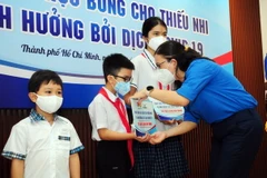 Lãnh đạo Đoàn thanh niên Thành phố Hồ Chí Minh cùng các mạnh thường quân tặng học bổng cho các em học sinh mồ côi do dịch COVID-19. (Ảnh: Thanh Vũ/TTXVN)