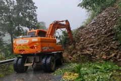 Lực lượng chức năng triển khai phương tiện máy móc tiến hành khắc phục sạt lở đất gây ách tắc giao thông. (Ảnh: TTXVN phát)