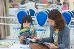 Học sinh và phụ huynh tranh thủ đọc sách, báo trong khi chờ thi tại trường Tiểu học Công nghệ Giáo dục Hà Nội. (Ảnh: CTV/Vietnam+)