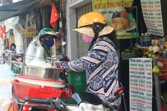 Các shipper tất bật với công việc giao các hàng ăn uống trên đường Đề Thám, quận 1, TP.HCM. (Ảnh: Thanh Vũ/TTXVN)