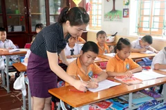 Giáo viên Tiểu học hướng dẫn học sinh làm bài tập. (Ảnh: Nguyễn Lành/TTXVN)