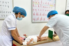 Nhân viên y tế đo chiều cao, cân nặng cho trẻ em. (Ảnh: T.G/Vietnam+)