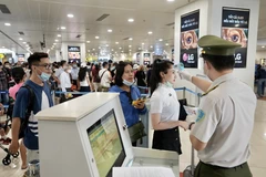 Kiểm tra thông tin cá nhân của hành khách và đo thân nhiệt trước khi vào điểm soi chiếu. (Ảnh: CTV/Vietnam+)