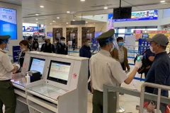 Nhân viên an ninh hàng không được trang bị đầy đủ găng tay, khẩu trang, tấm chắn giọt bắn trong khi đo thân nhiệt cho hành khách. (Ảnh: CTV/Vietnam+)