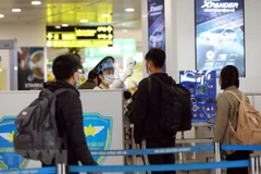 Nhân viên an ninh hàng không tại sân bay Nội Bài kiểm tra thân nhiệt của hành khách. (Ảnh: Huy Hùng/TTXVN)