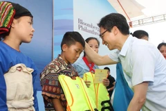 Phó Thủ tướng Chính phủ Vũ Đức Đam tặng áo phao cho các em nhỏ tại buổi lễ. (Ảnh: Thanh Tùng/TTXVN)