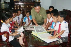 Ông Đào Thông giới thiệu bộ sưu tầm về Bác Hồ cho học sinh trường Tiểu học số 2-Bảo Ninh, tỉnh Quảng Bình. (Ảnh: Ngọc Châu/Vietnam+)