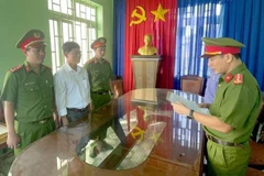Công an đọc lệnh khởi tố bị can, bắt tạm giam đối với Phạm Đình Nhất (áo trắng). (Ảnh: TTXVN phát)