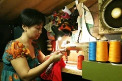 Chị Thủy cặm cụi đính cườm chiếc áo cho Quân kịp mặc diễn show buổi tối. (Ảnh: Cẩm Thơ/ Vietnam+)