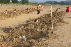 Nhóm du khách nằm dưới các hố cát tự đào trên bãi biển Cửa Lò. (Ảnh cắt từ clip).